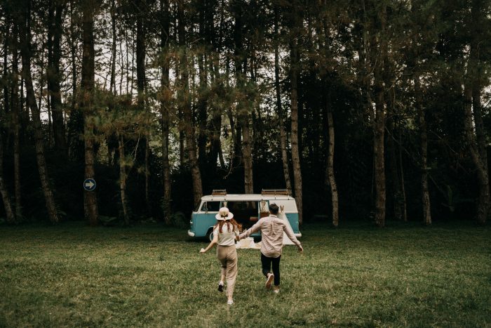 couple hand in hand running towards vintage VW bus