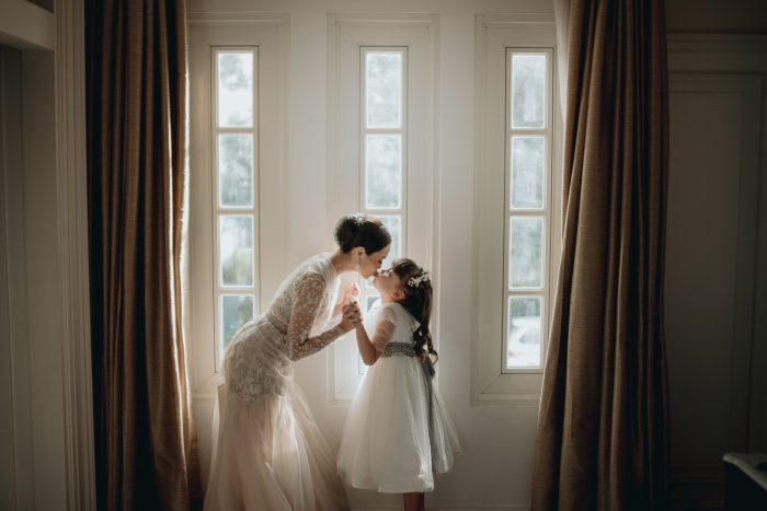 bride and flower girl kissing in front of window