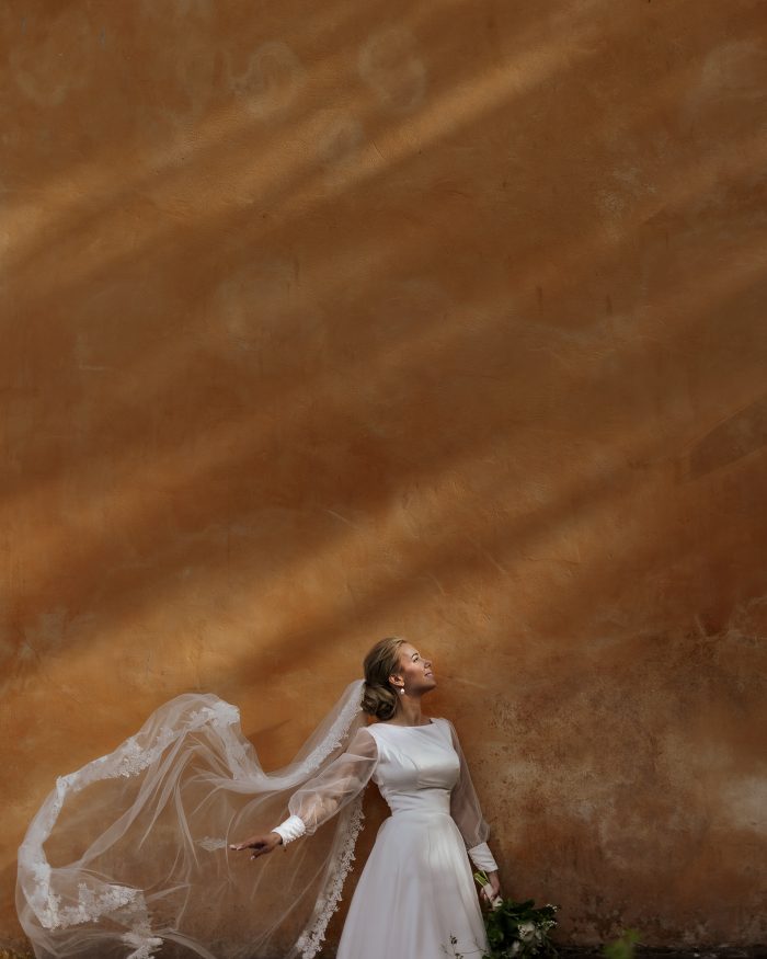 bride in long-sleeve gown veil blowing in wind