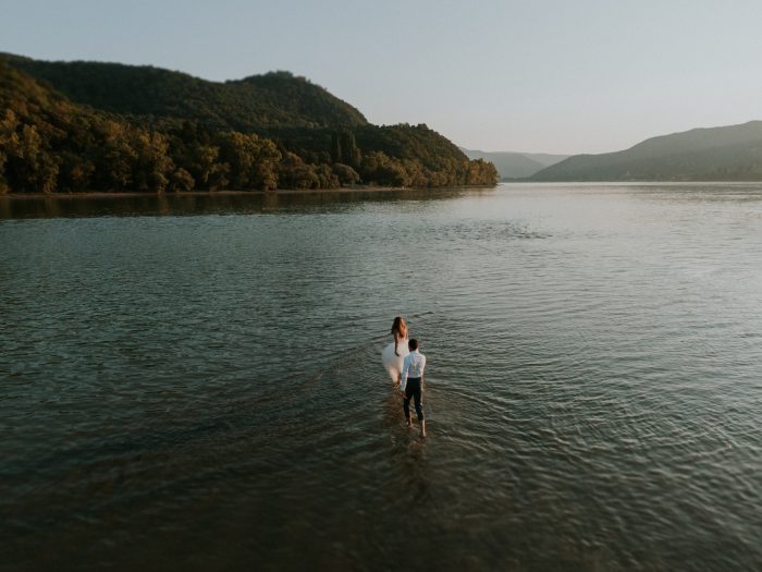 photo couple holding hands walking through lake
