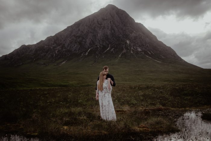 moody wide shot of couple in front of Scotland mountain
