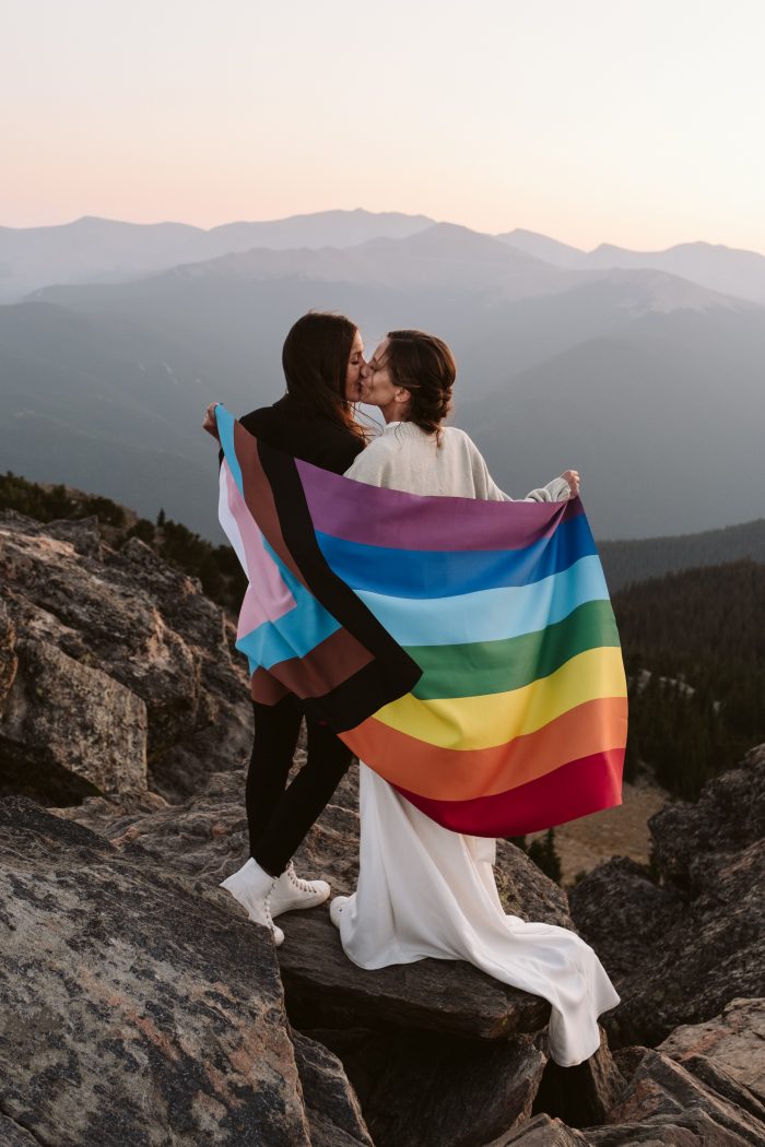 same-sex couple celebrates on mountain with LGBTQ flag