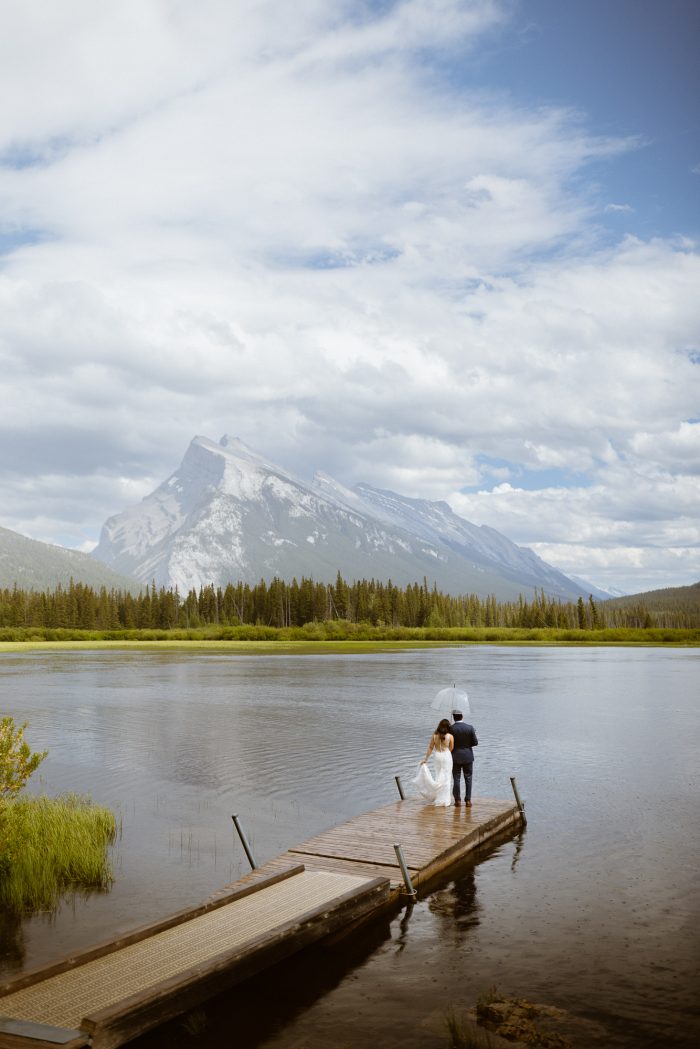 wedding day couple on dock looking at mountains in Banff
