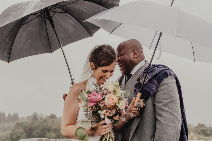 Scottish bride and groom laughing while holding umbrellas