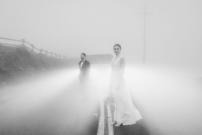 portrait of wedding couple in street using car headlights