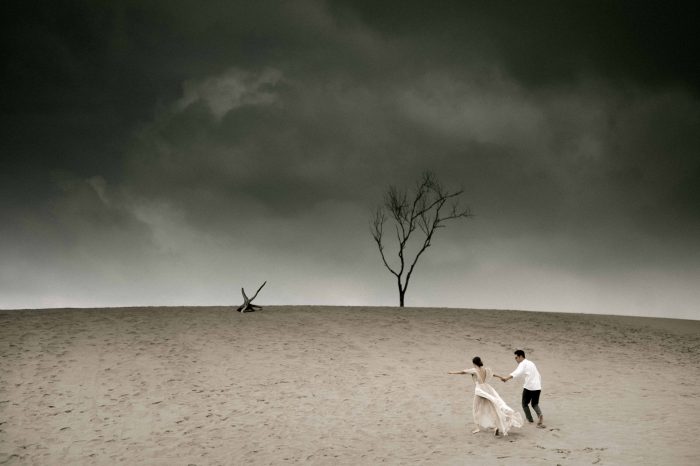 wedding couple running across sand under dark sky