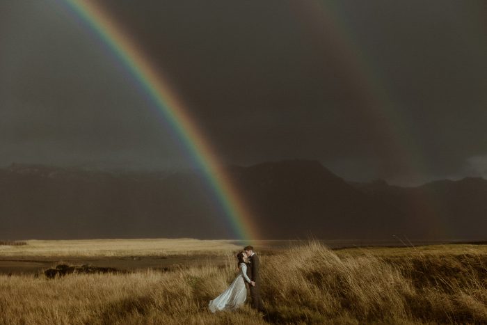 wedding couple kissing underneath rainbow