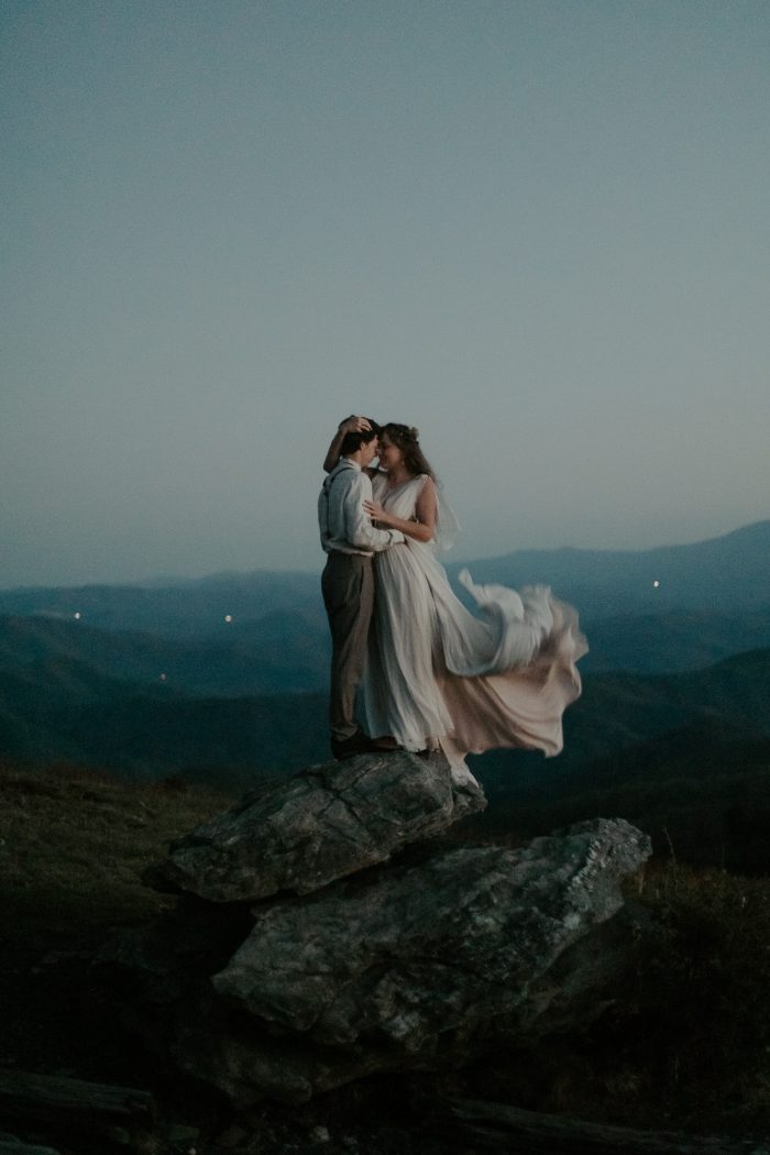 blue hour photo of wedding day couple standing on rock 