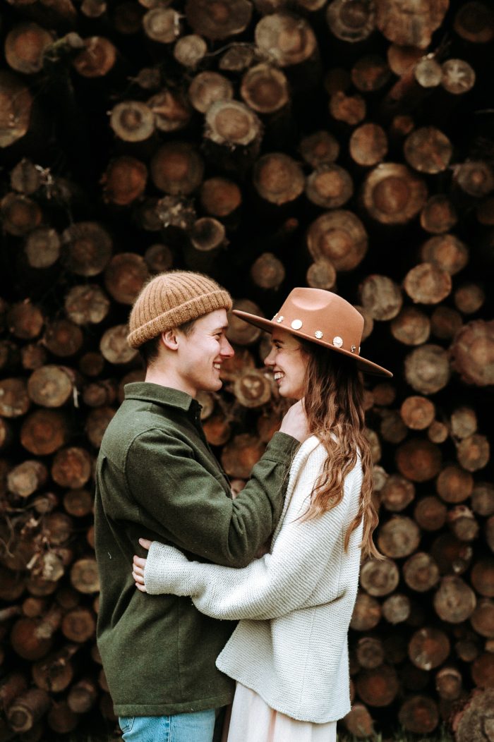 casual engagement photo with hats and stack of logs
