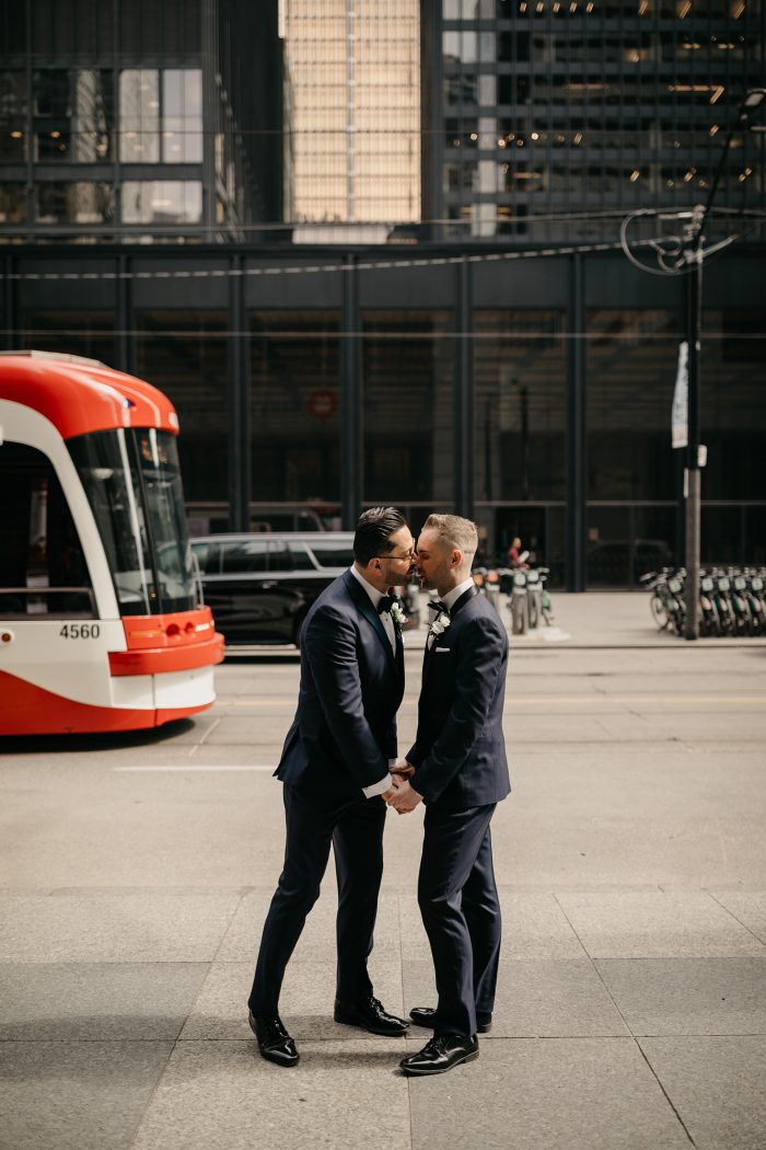 same-sex couple in tailored suits kissing on city street