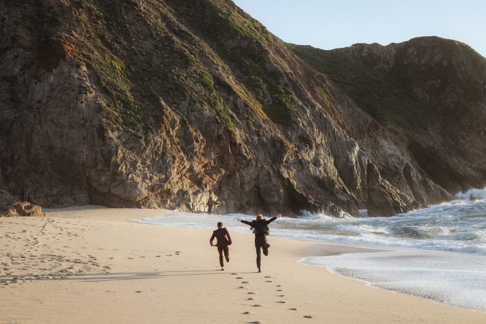 newly engaged couple running through gray whale cove state park