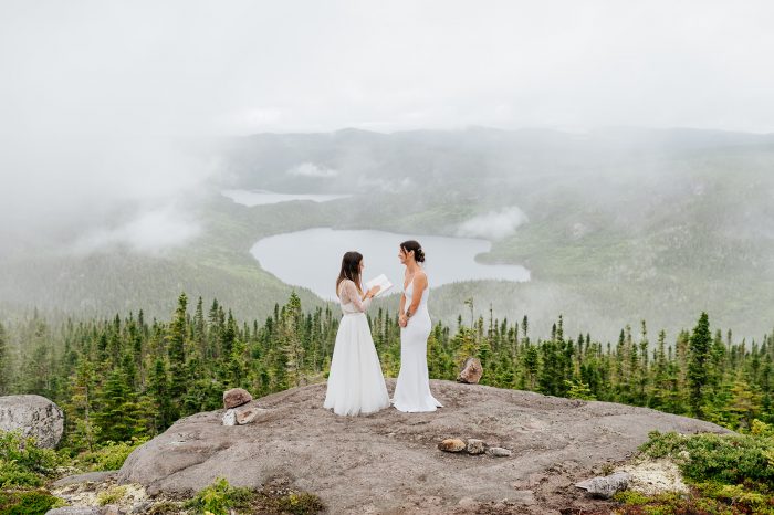 two brides reading wedding vows on top of mountain
